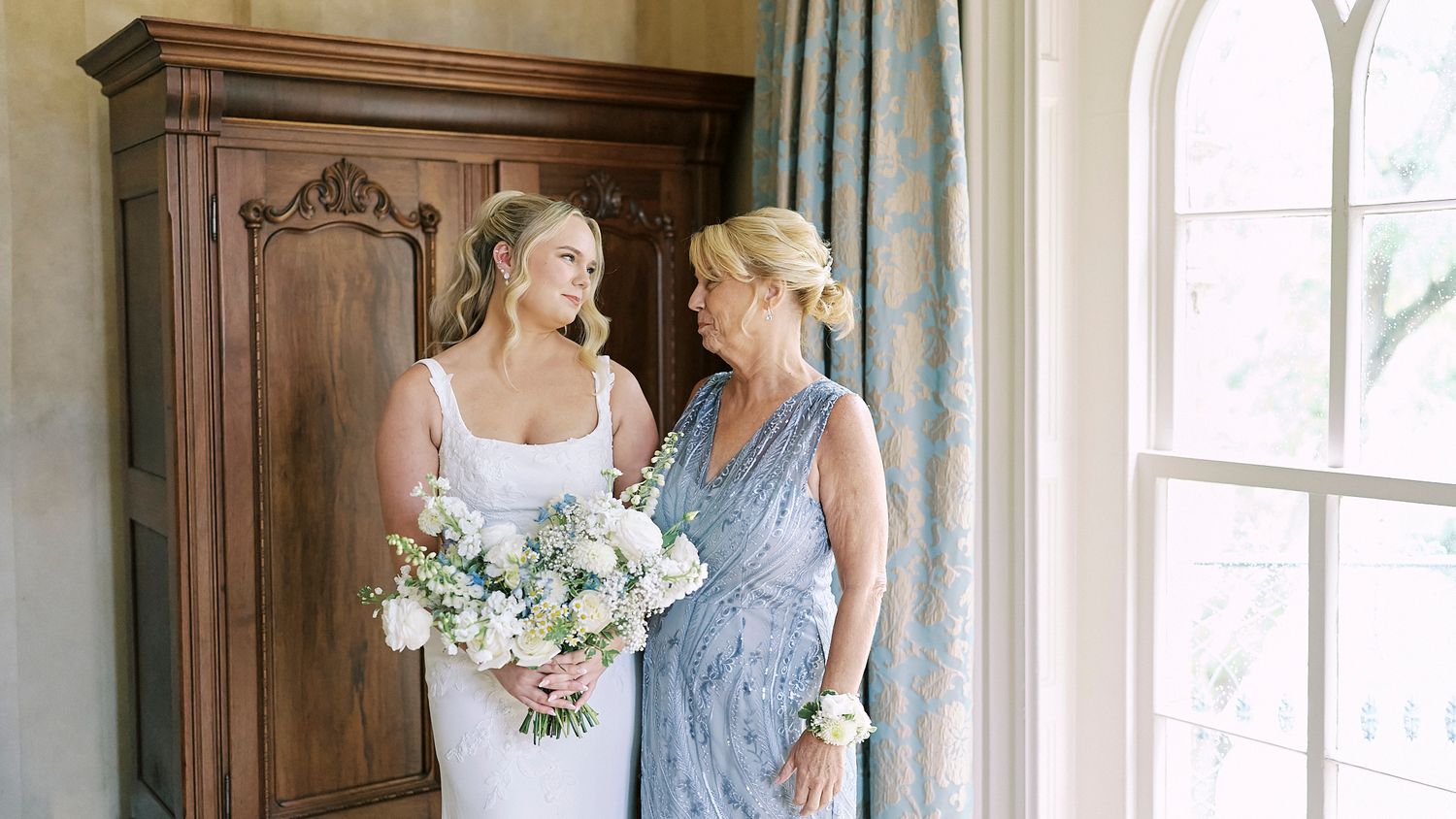 Elegant bridal party in light blue dresses poses near sunlit windows in grand room.
