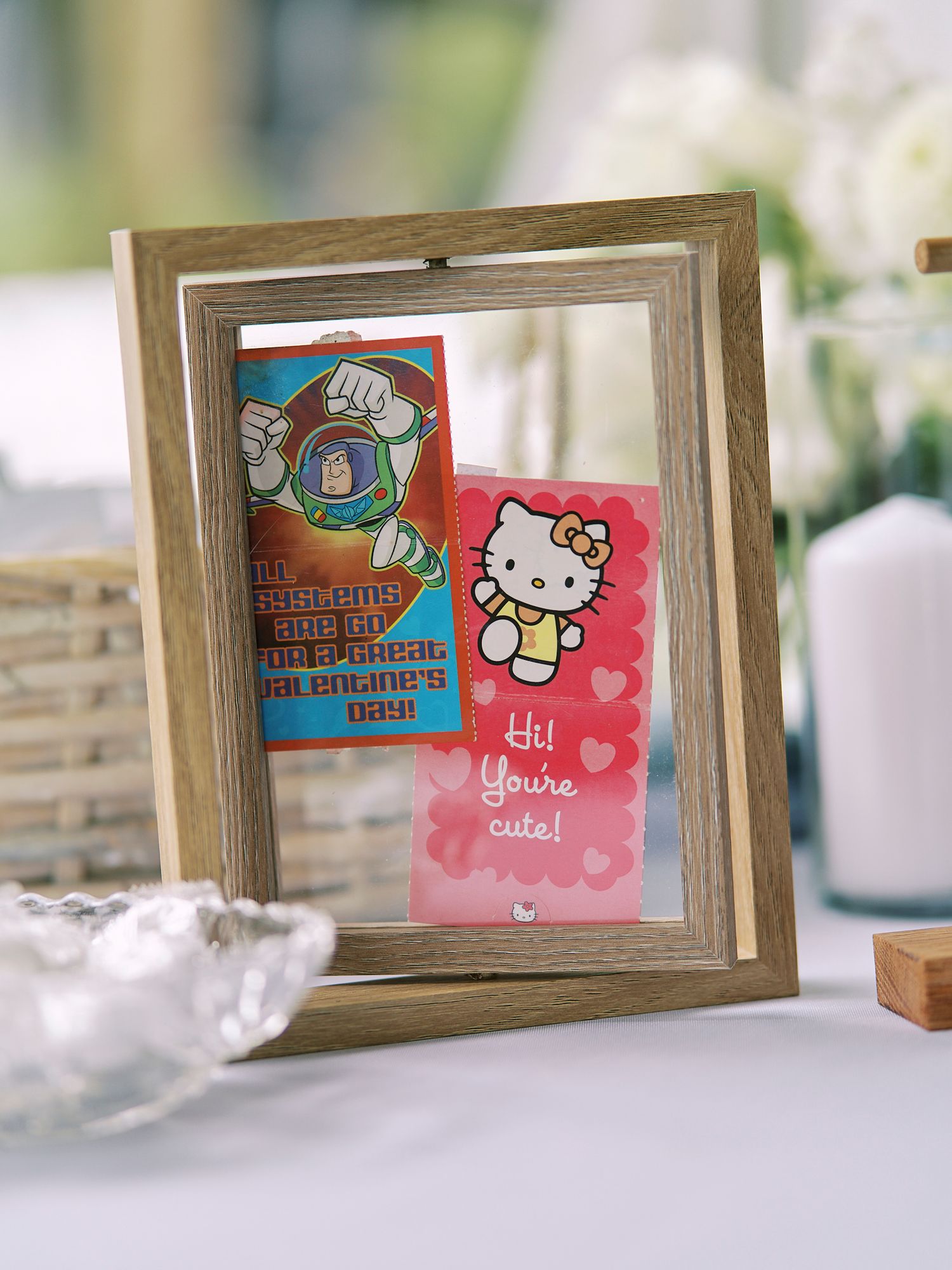 Three rustic wooden frames displaying pink Hello Kitty greeting cards and stickers in a soft focus setting.