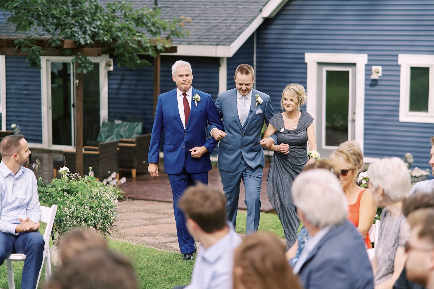 Wedding guests gather in front of a navy blue house for an intimate outdoor ceremony.