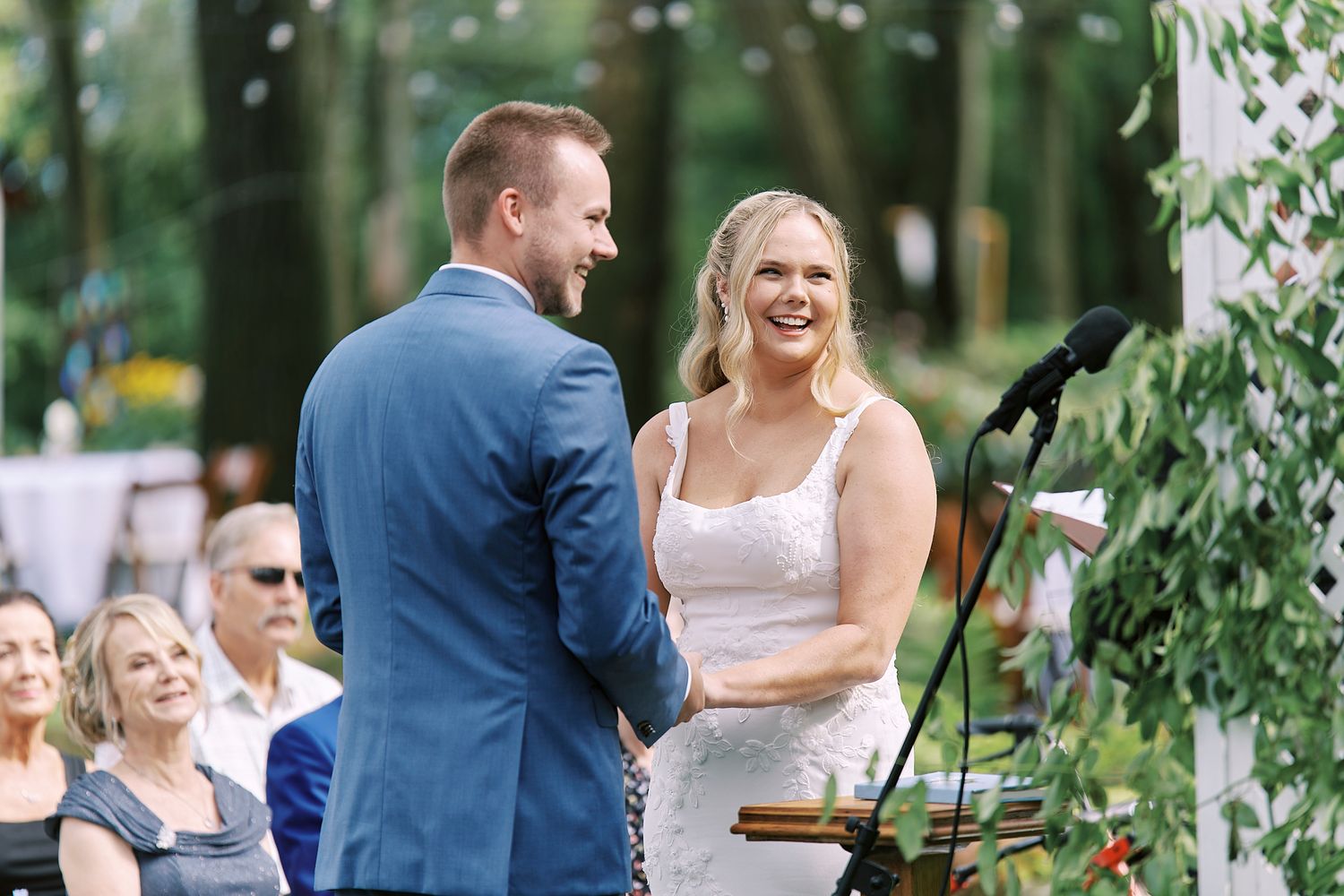 Wedding ceremony guests share joyful moments in an outdoor garden setting under green foliage.