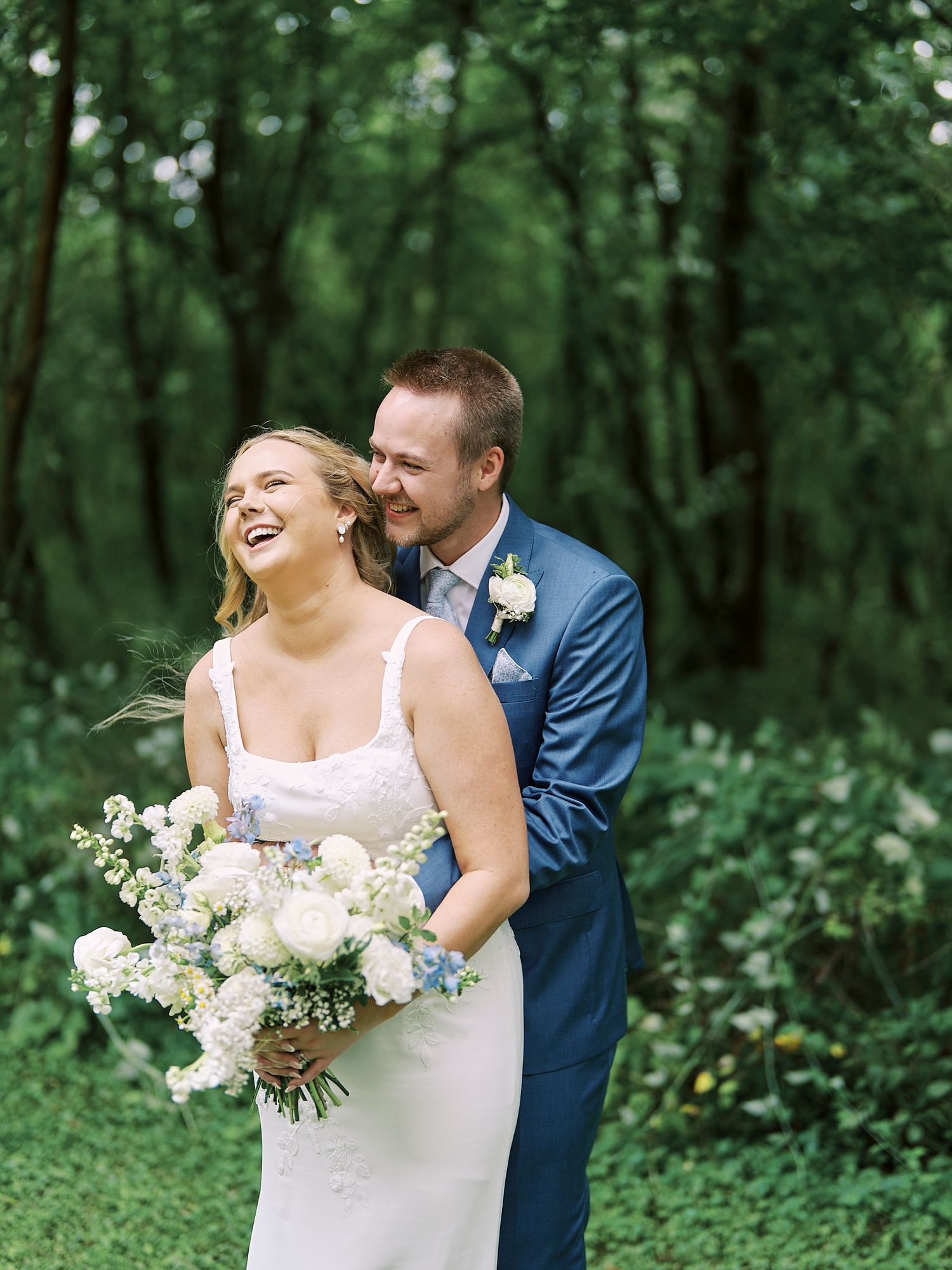 Joyful couple shares a candid moment during their outdoor wedding photo session surrounded by lush greenery.