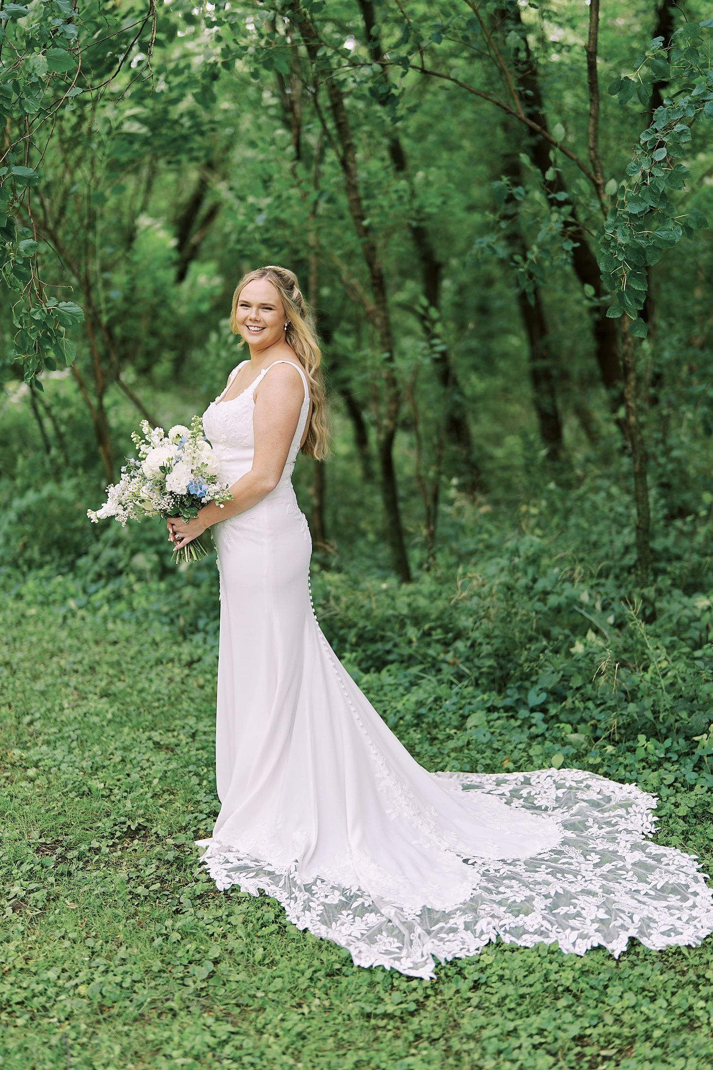 White lace wedding dress with a flowing train photographed in a serene forest setting.