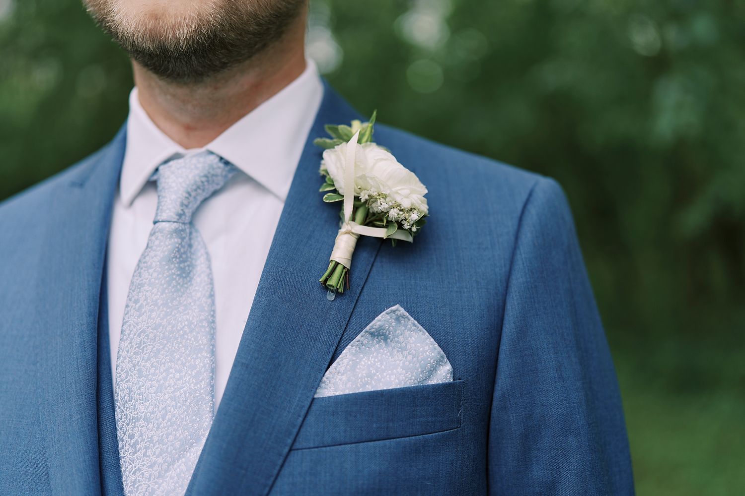 A light pink boutonniere made with delicate flowers and greenery adorns a navy blue suit lapel.