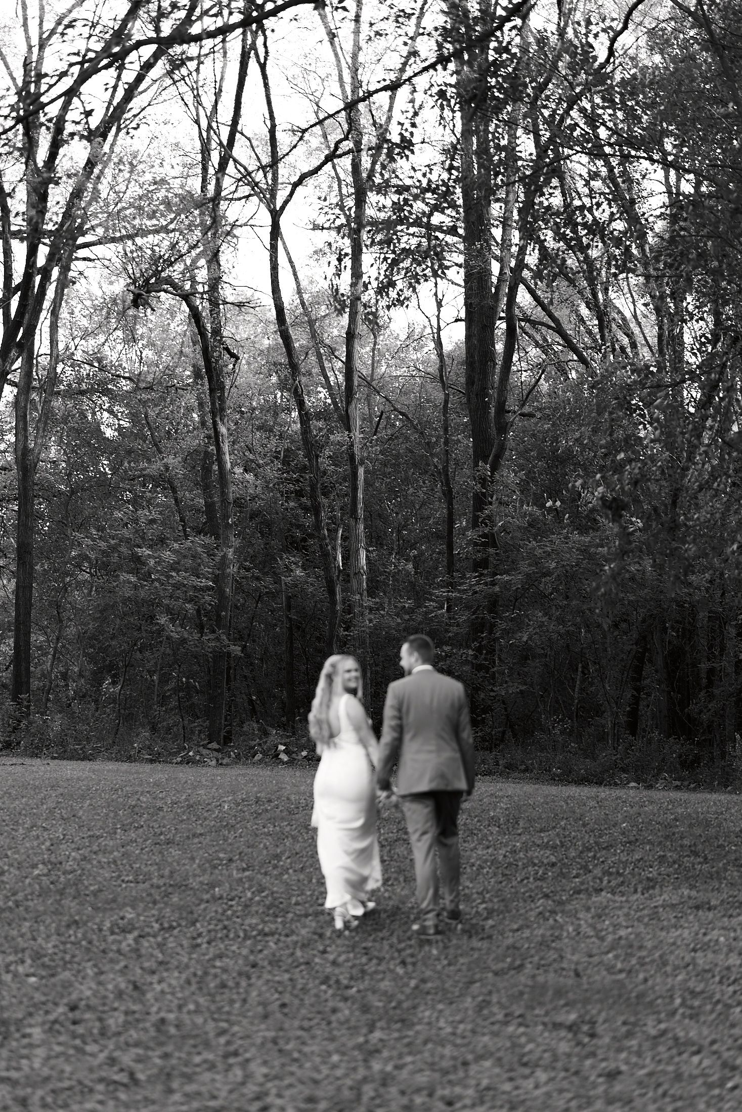 Black and white wedding photo sequence showing couple walking through a grassy field near trees.
