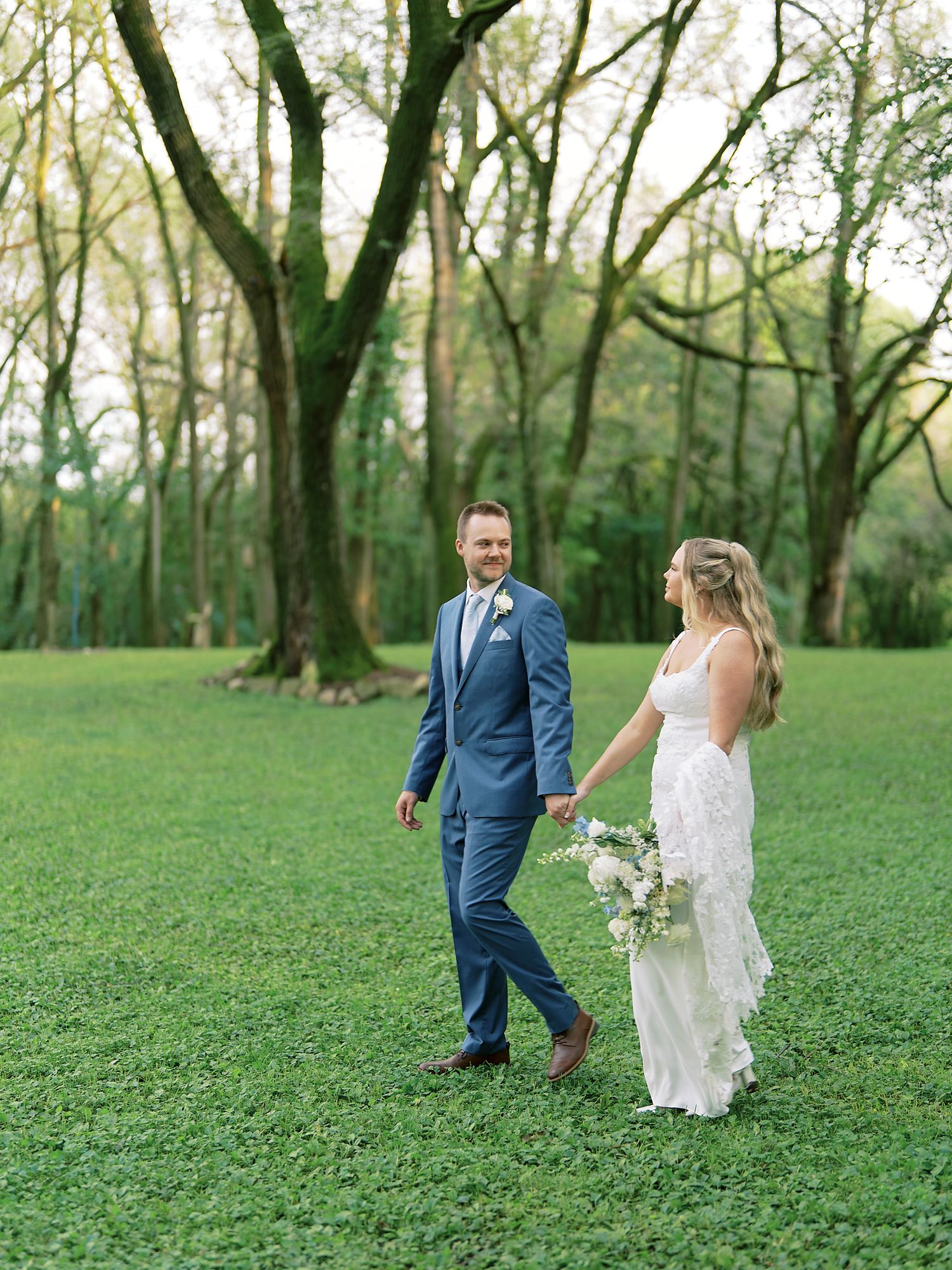 Couple walking through a green woodland area during their outdoor wedding photoshoot.