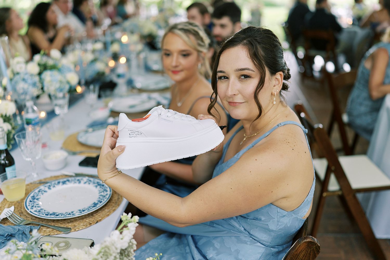 People gather around decorated tables at an elegant outdoor event with blue and white place settings.