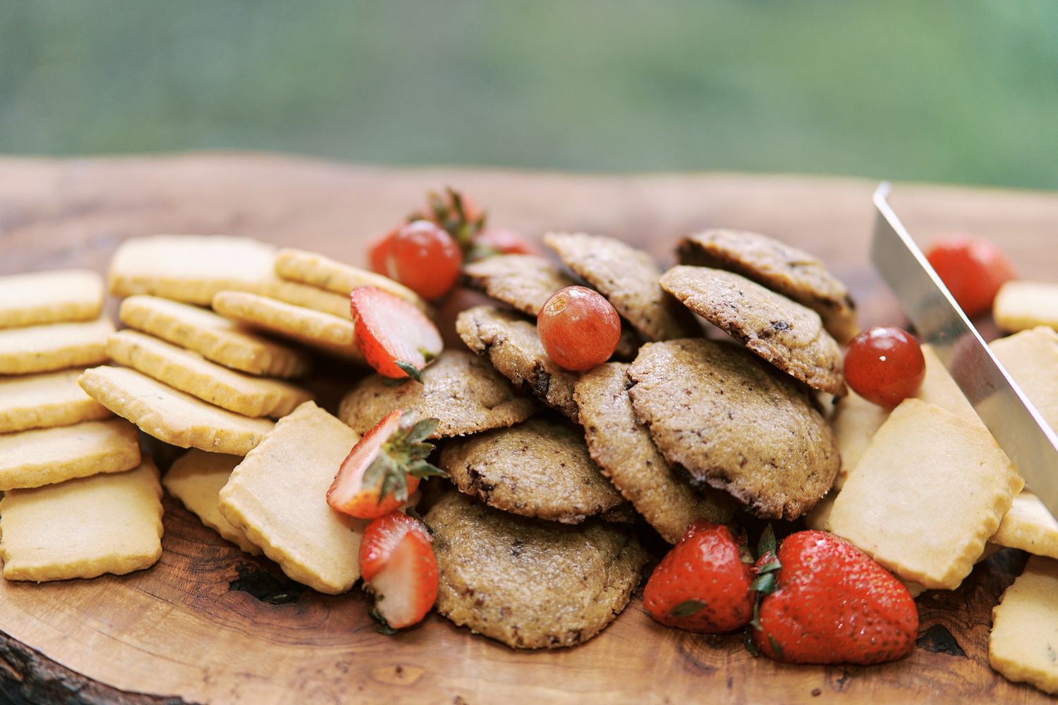 Freshly baked chocolate chip cookies with fresh strawberries arranged on a wooden cutting board.