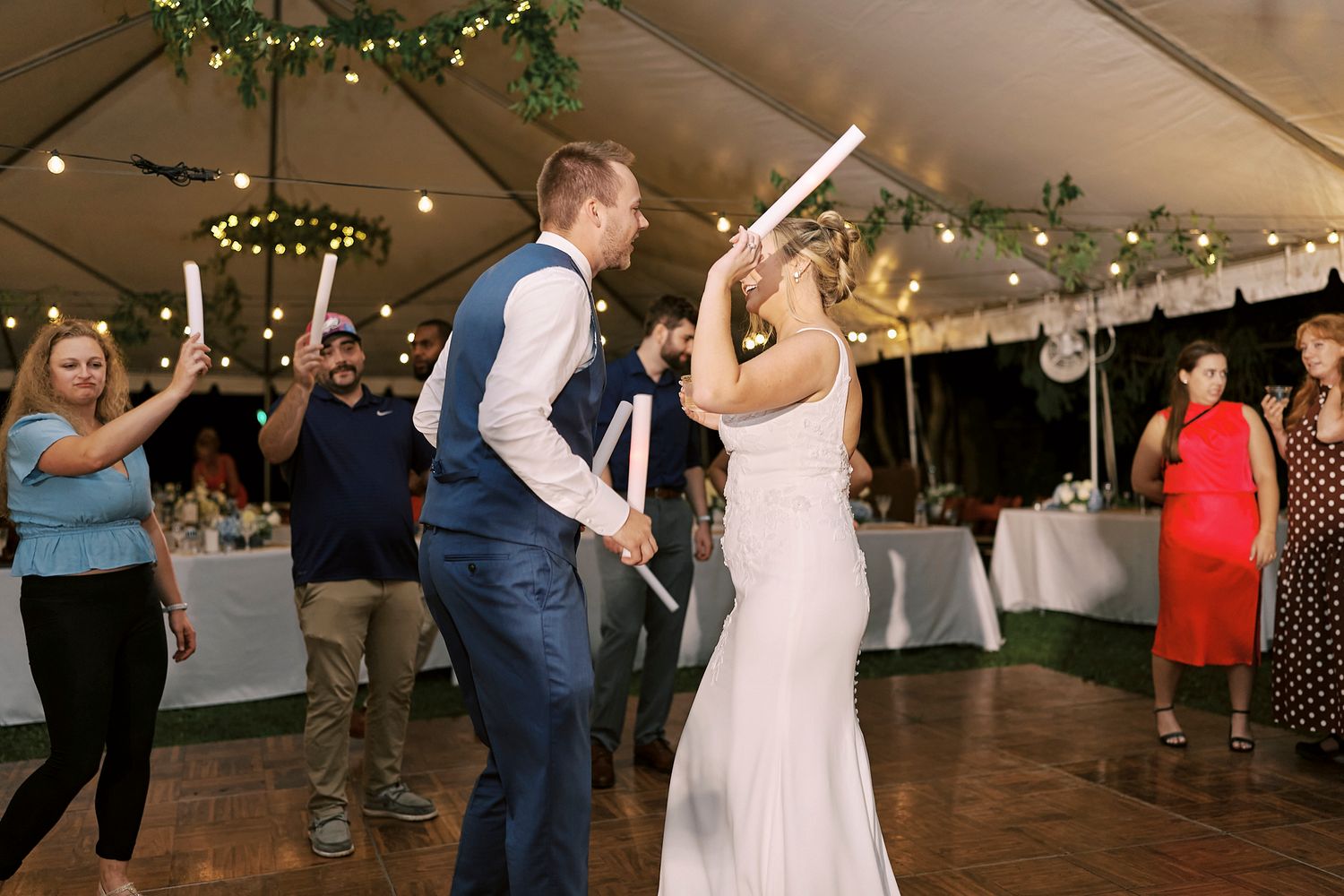 Wedding celebration on a dance floor with guests dancing under twinkling lights at an outdoor tent reception.