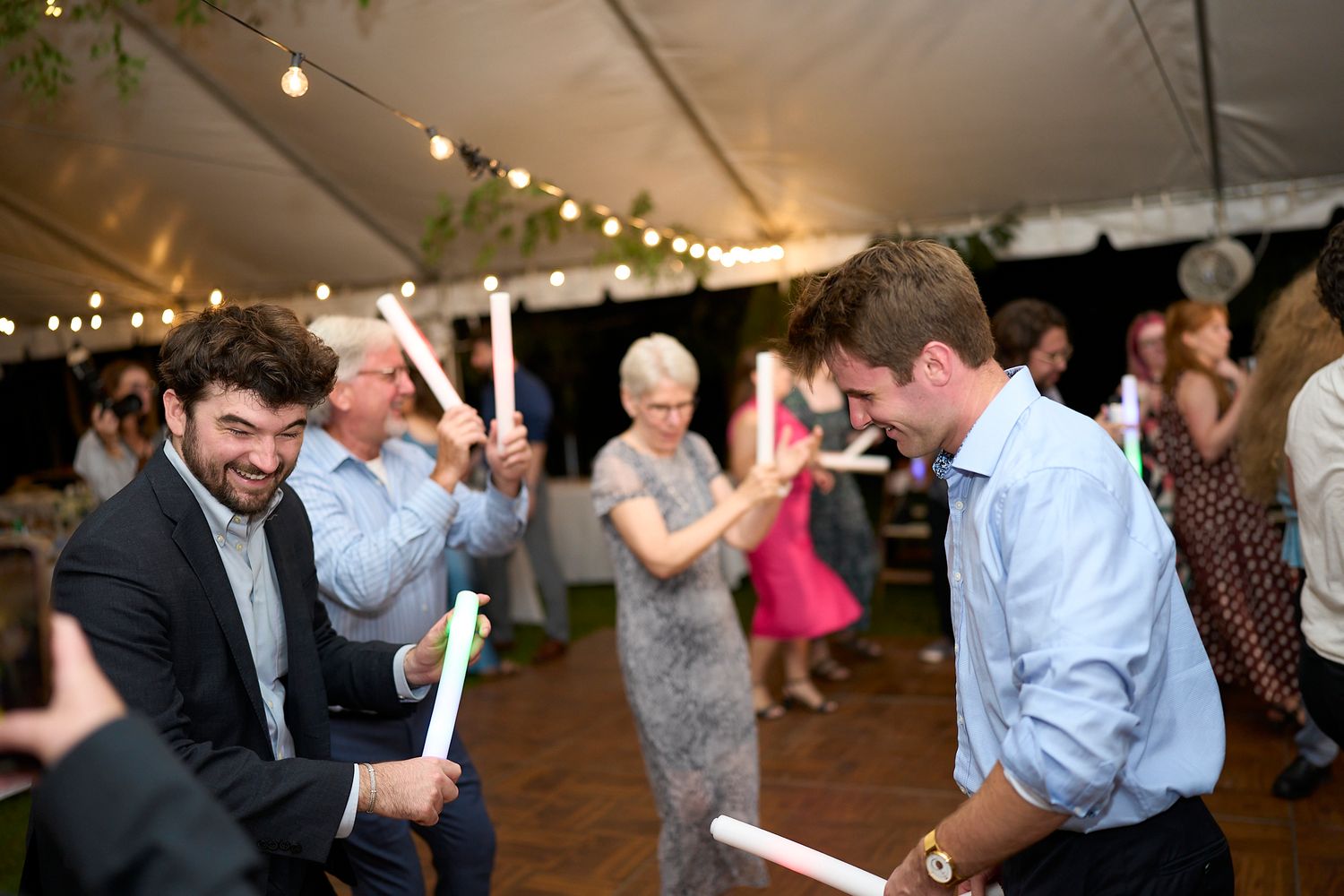 Festive dance party atmosphere with string lights illuminating guests celebrating at an evening wedding reception.