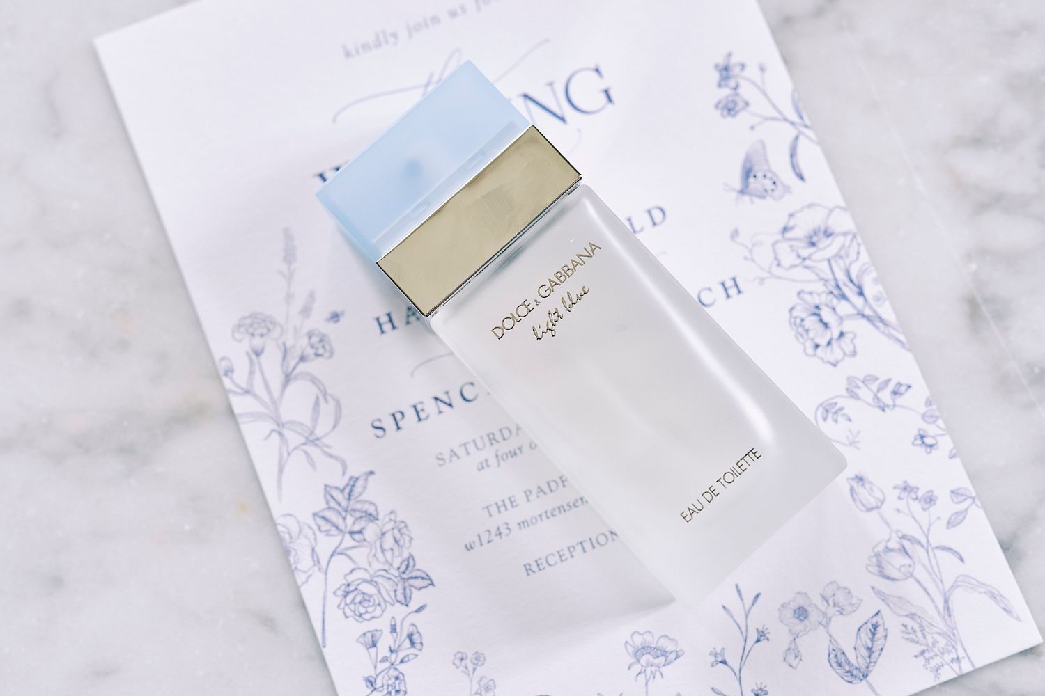 White and purple floral cosmetic product packaging arranged elegantly on a marble surface.
