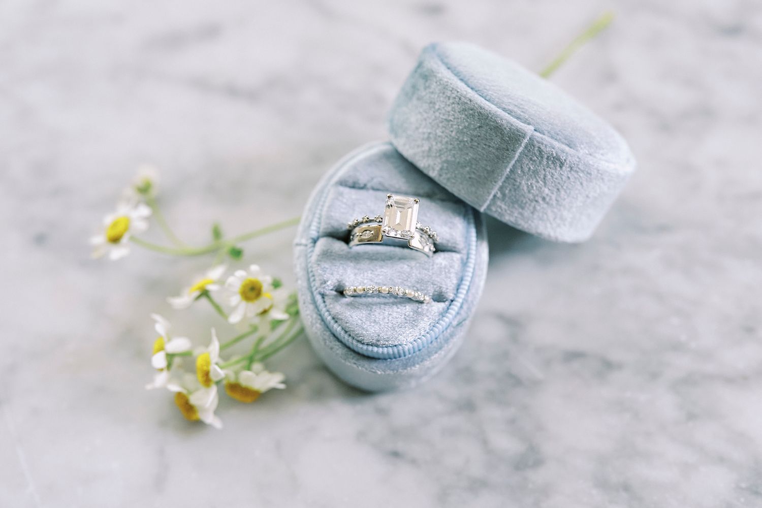Delicate rose gold engagement ring in light blue velvet ring box with small white flowers on marble surface.