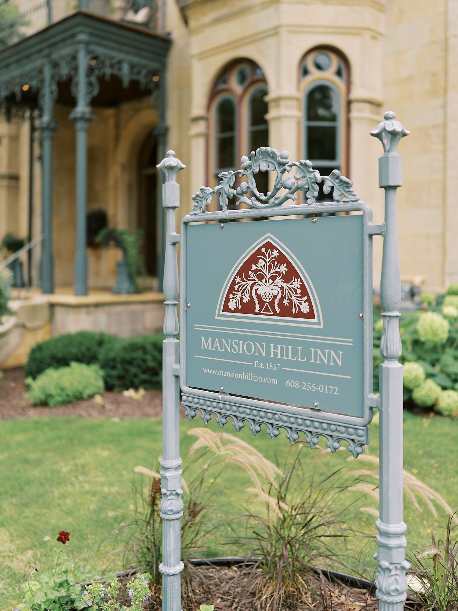 Ornate vintage signs for Mansion Hill Inn displayed on decorative posts with elaborate scrollwork in muted teal and gold colors.