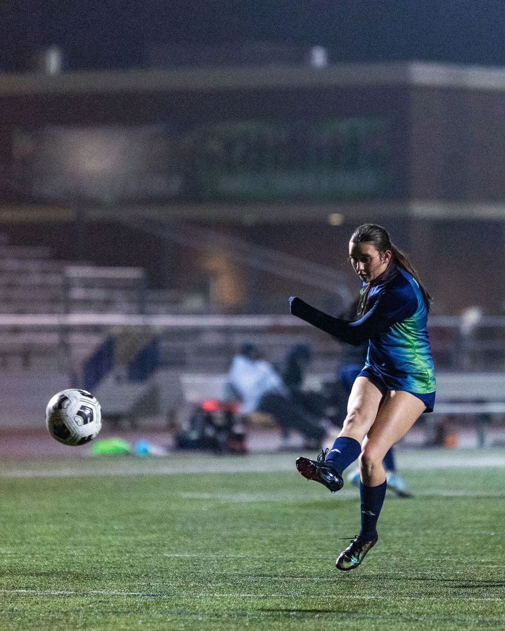 Soccer player performing a sliding kick on grass field with dramatic lighting at dusk.