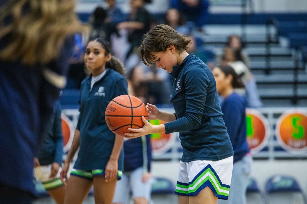 Two basketball players practice dribbling drills during a team training session in a gymnasium.