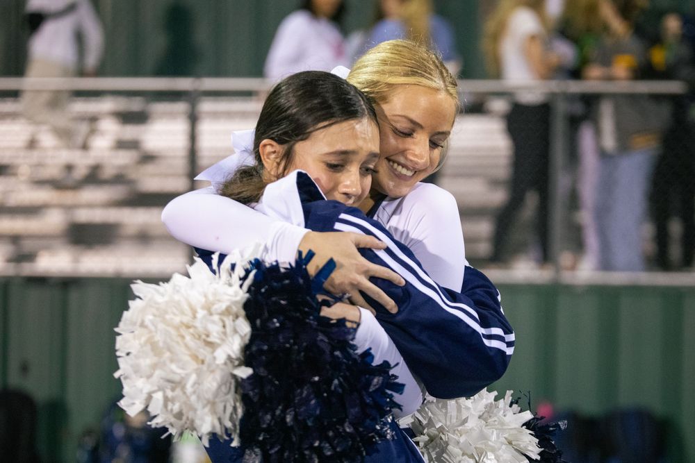 Navy and white cheerleaders perform synchronized dance moves at a sporting event.