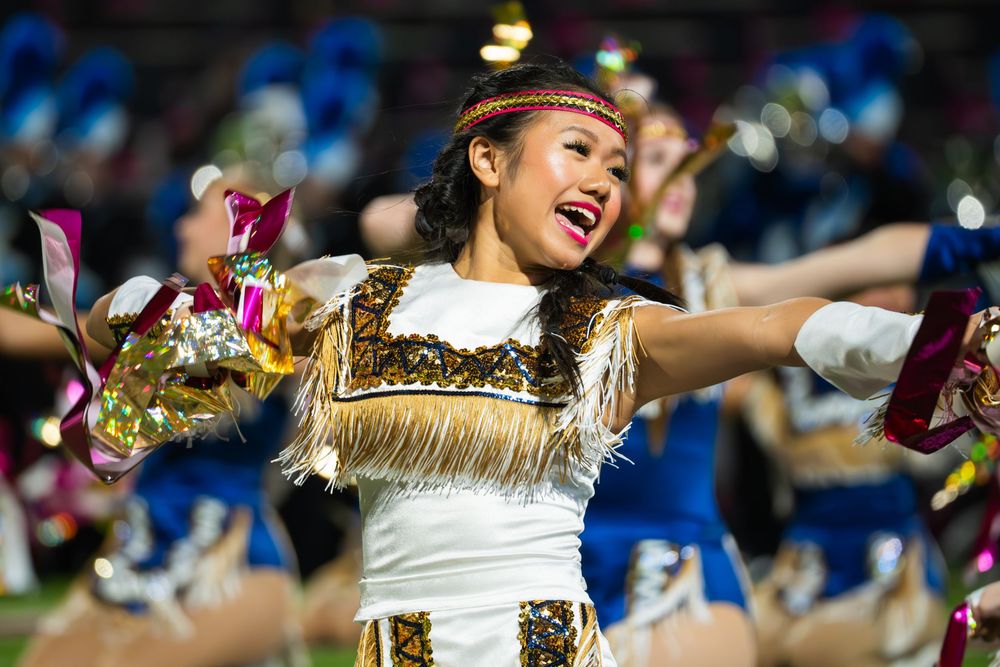 Cheerleaders perform a synchronized dance routine while wearing white and gold uniforms at a sporting event.