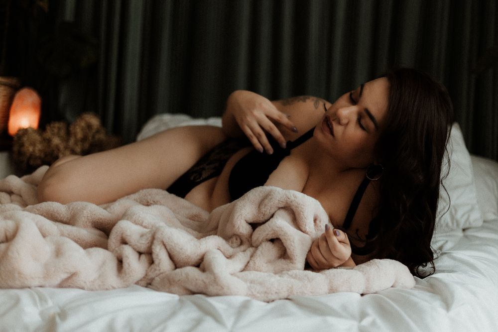Intimate boudoir photography session with soft lighting and white bedding creating sensual atmosphere.