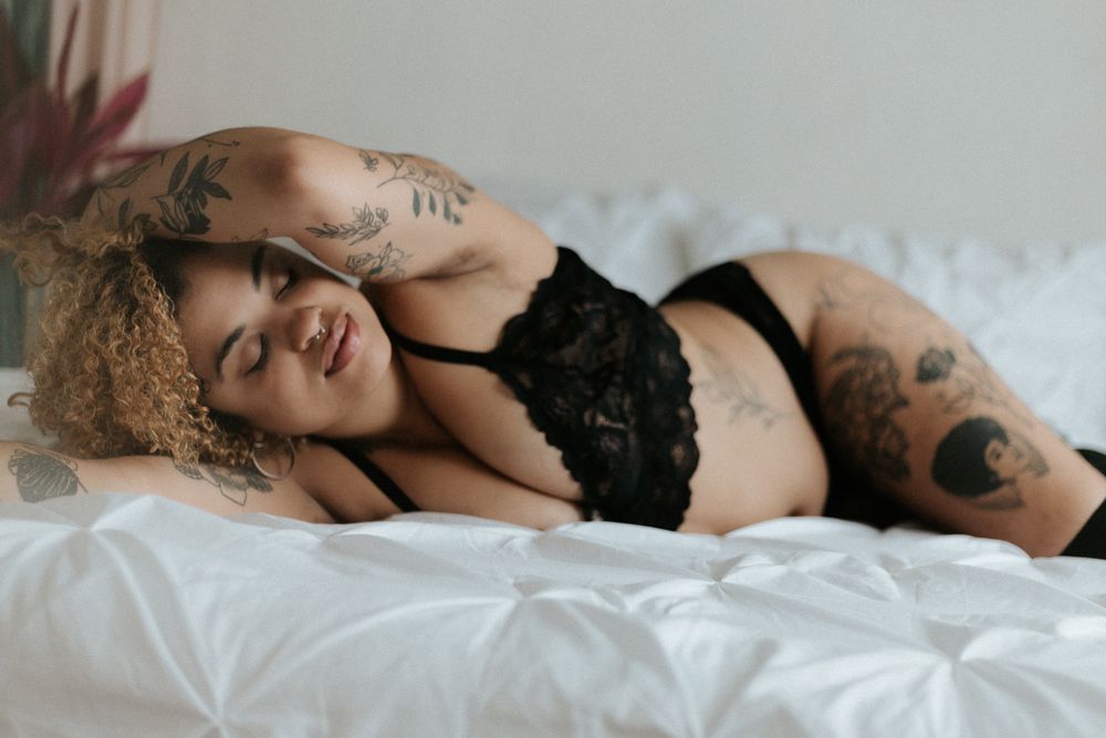 Intimate portrait of person with curly hair wearing black lace lingerie on white bedding.