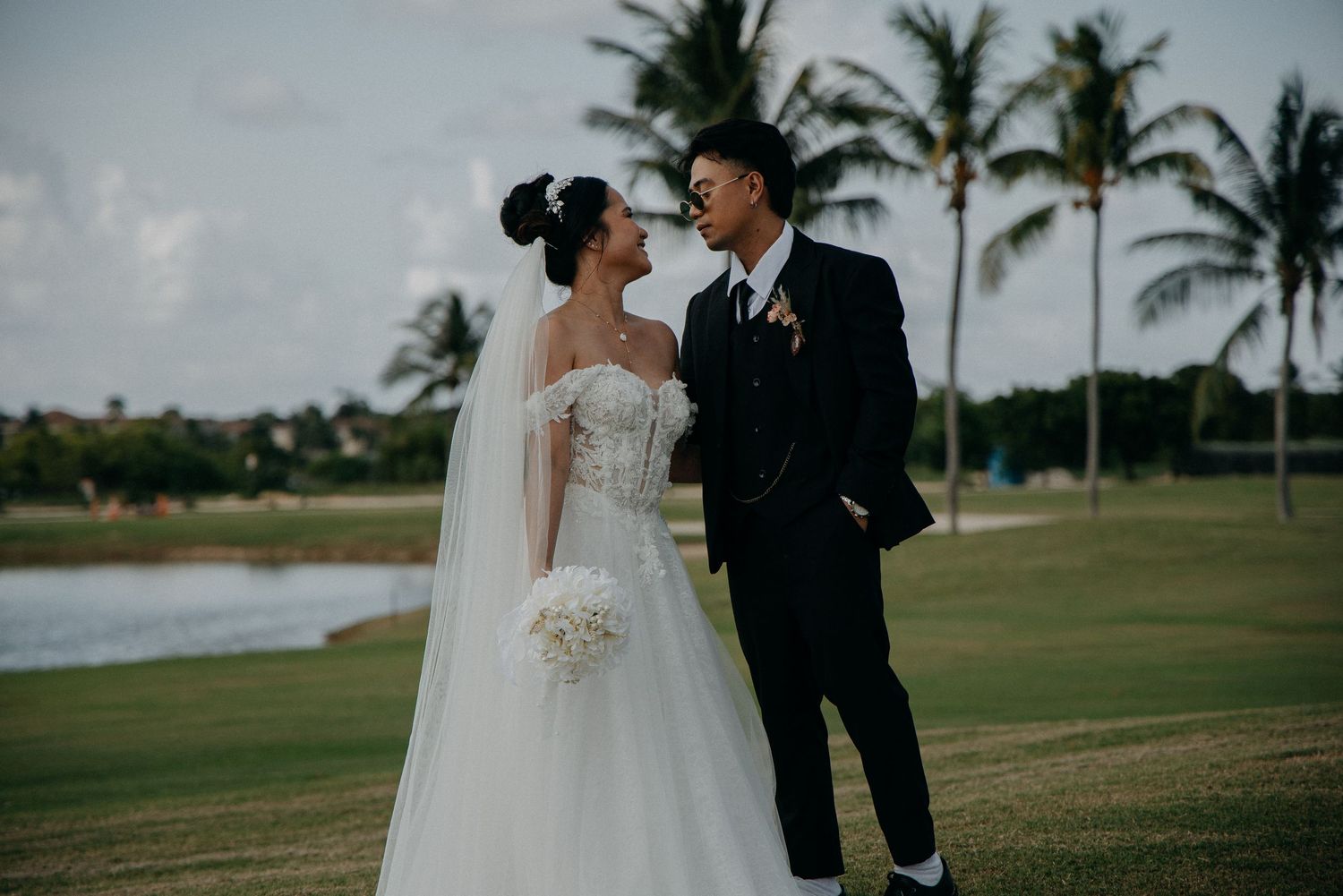 Wedding couple embracing on a palm-lined golf course with cloudy skies.