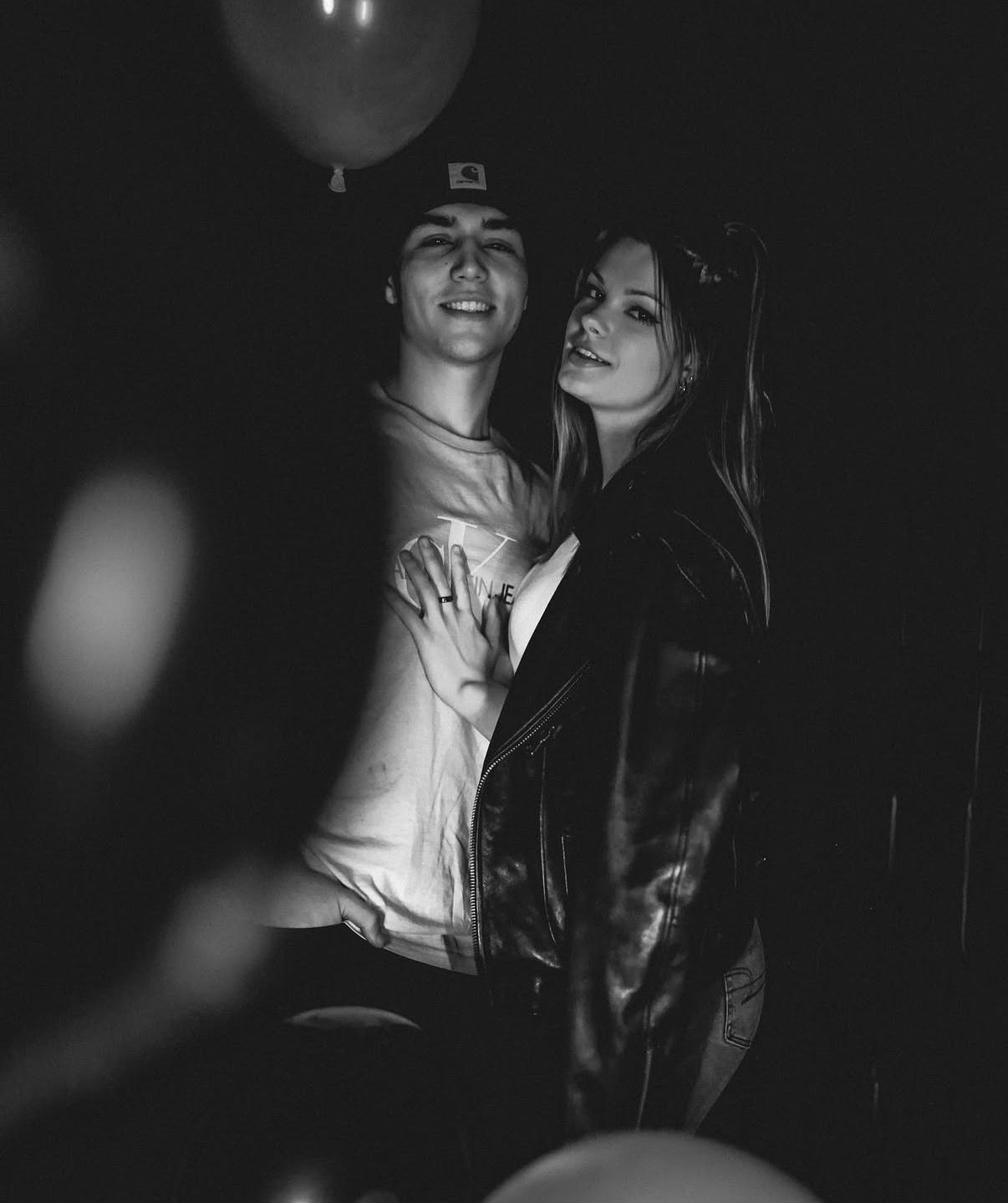 A romantic couple shares an intimate monochrome moment together in dim lighting with balloons in the background.