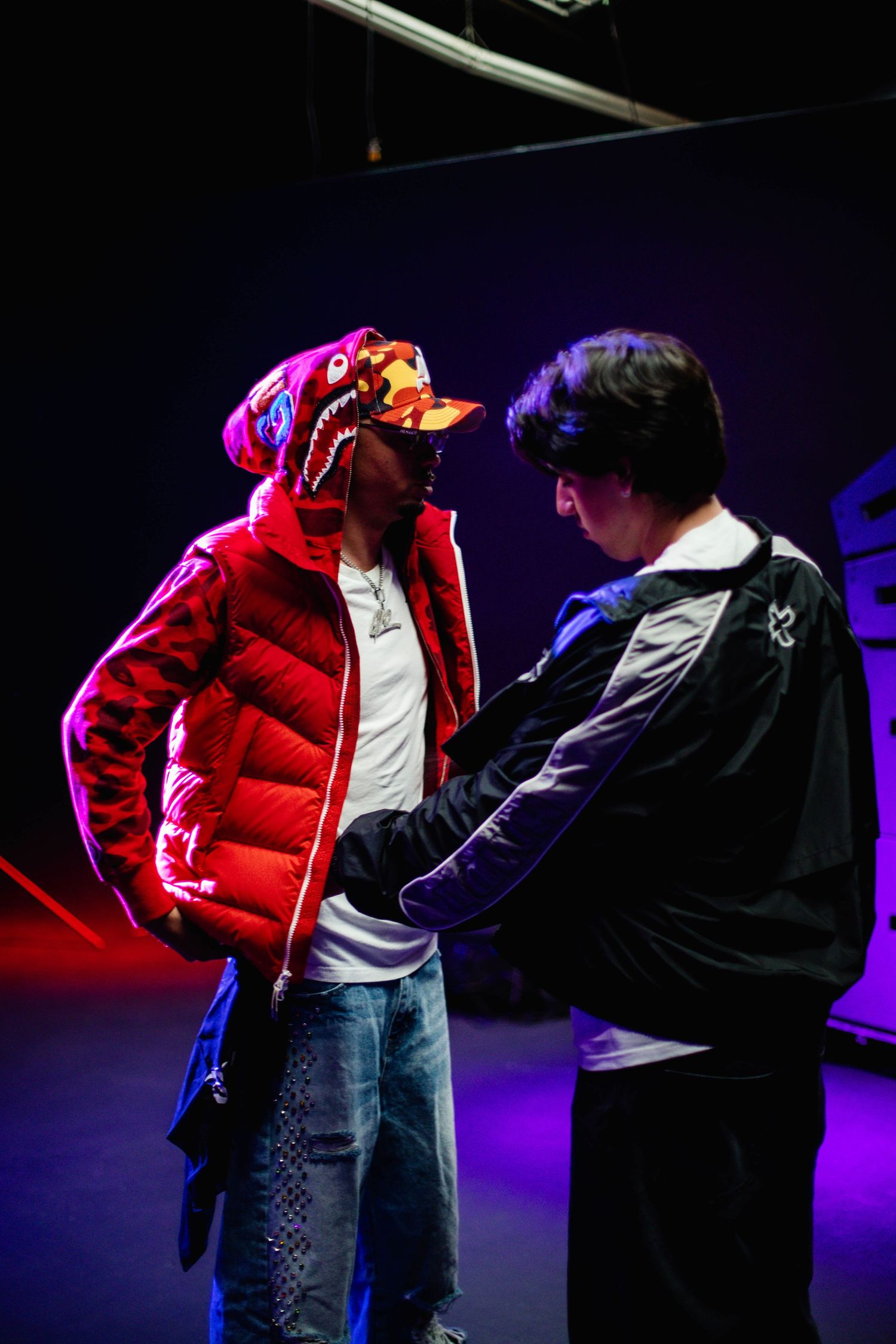 Two performers in a dramatic scene on a dark stage with purple and red lighting effects.