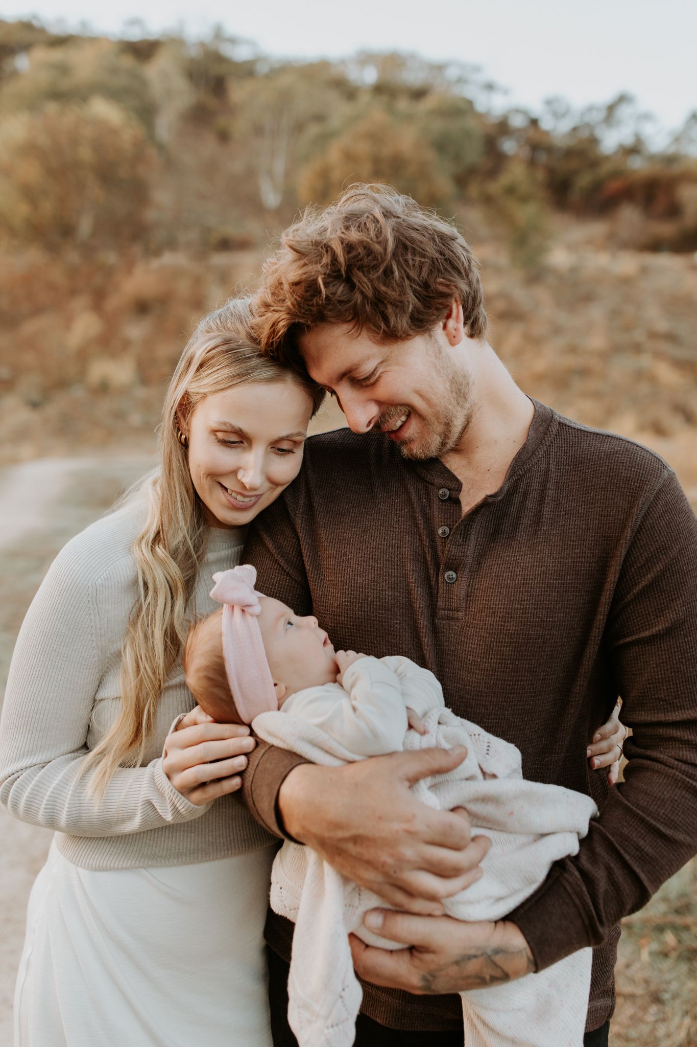 Adelaide newborn photographer captures tiny baby in soft wraps for serene photo session with Mum and Dad in a field at Sunrise.