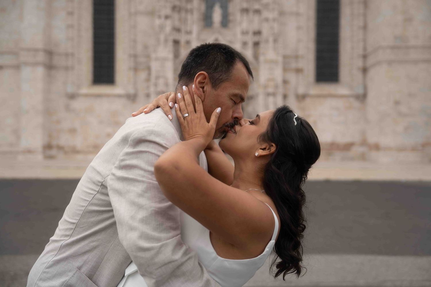 Intimate wedding portrait with couple embracing against stone church architecture.