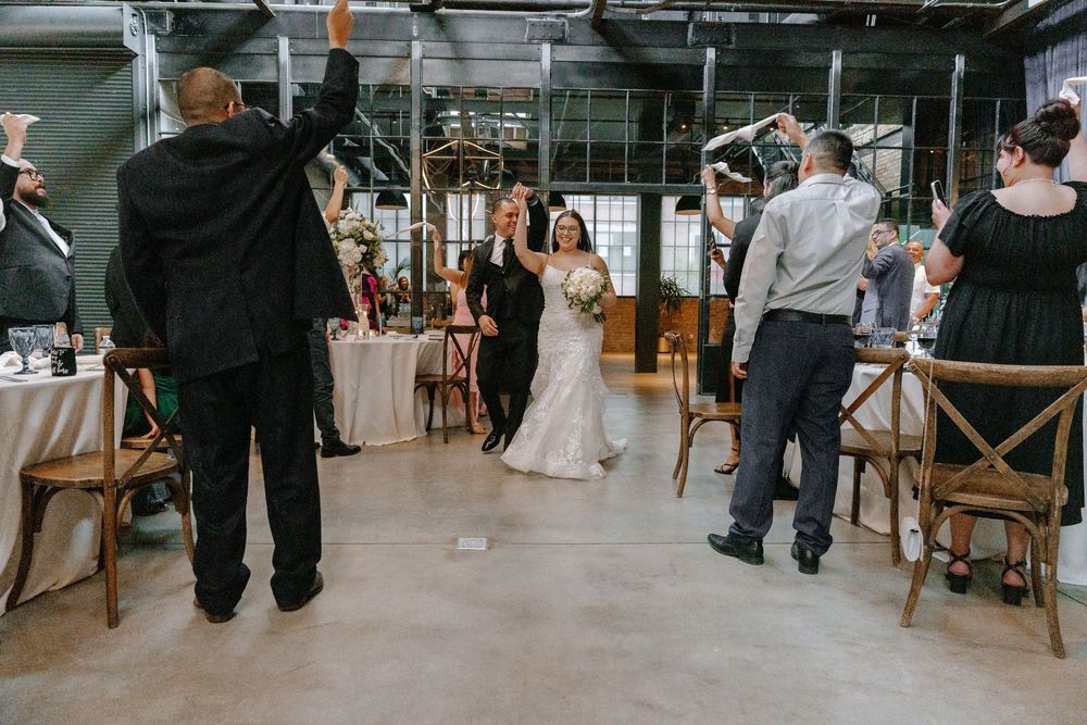 A couple celebrates their wedding ceremony in an industrial-style venue with rustic wooden chairs and exposed ceilings.