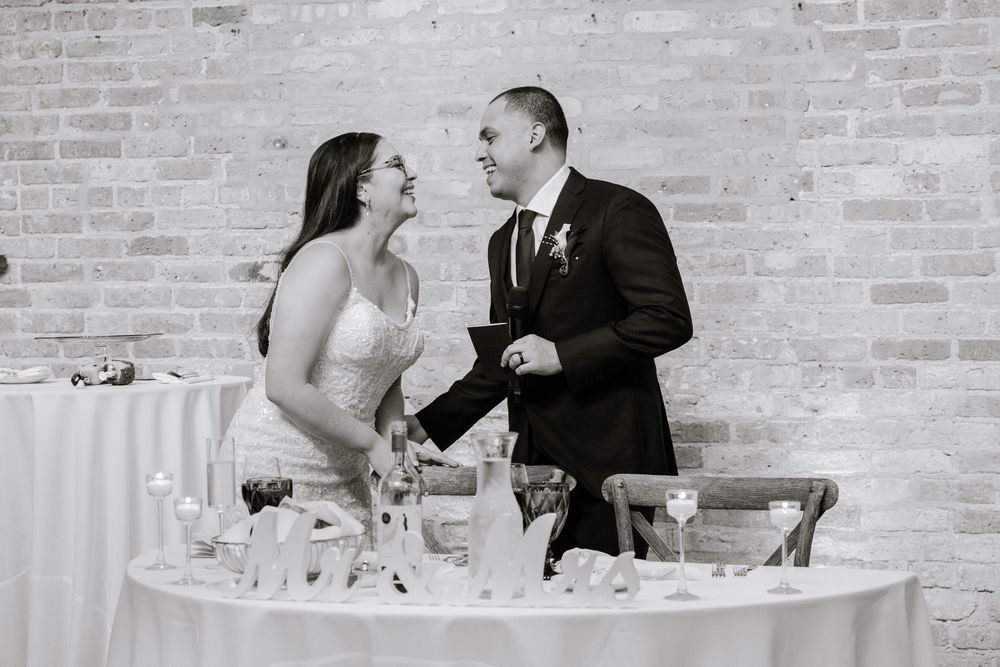 Guests enjoying a conversation at a modern reception with minimalist white table settings against exposed brick walls.