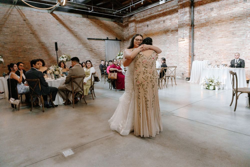 Two people dance closely together during a wedding reception in an industrial-style venue with exposed brick walls.