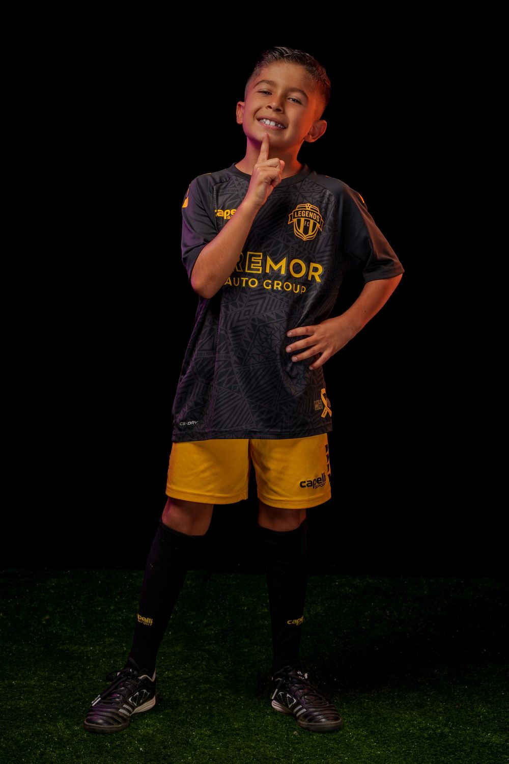 Soccer player in dark uniform poses energetically on green turf at night.