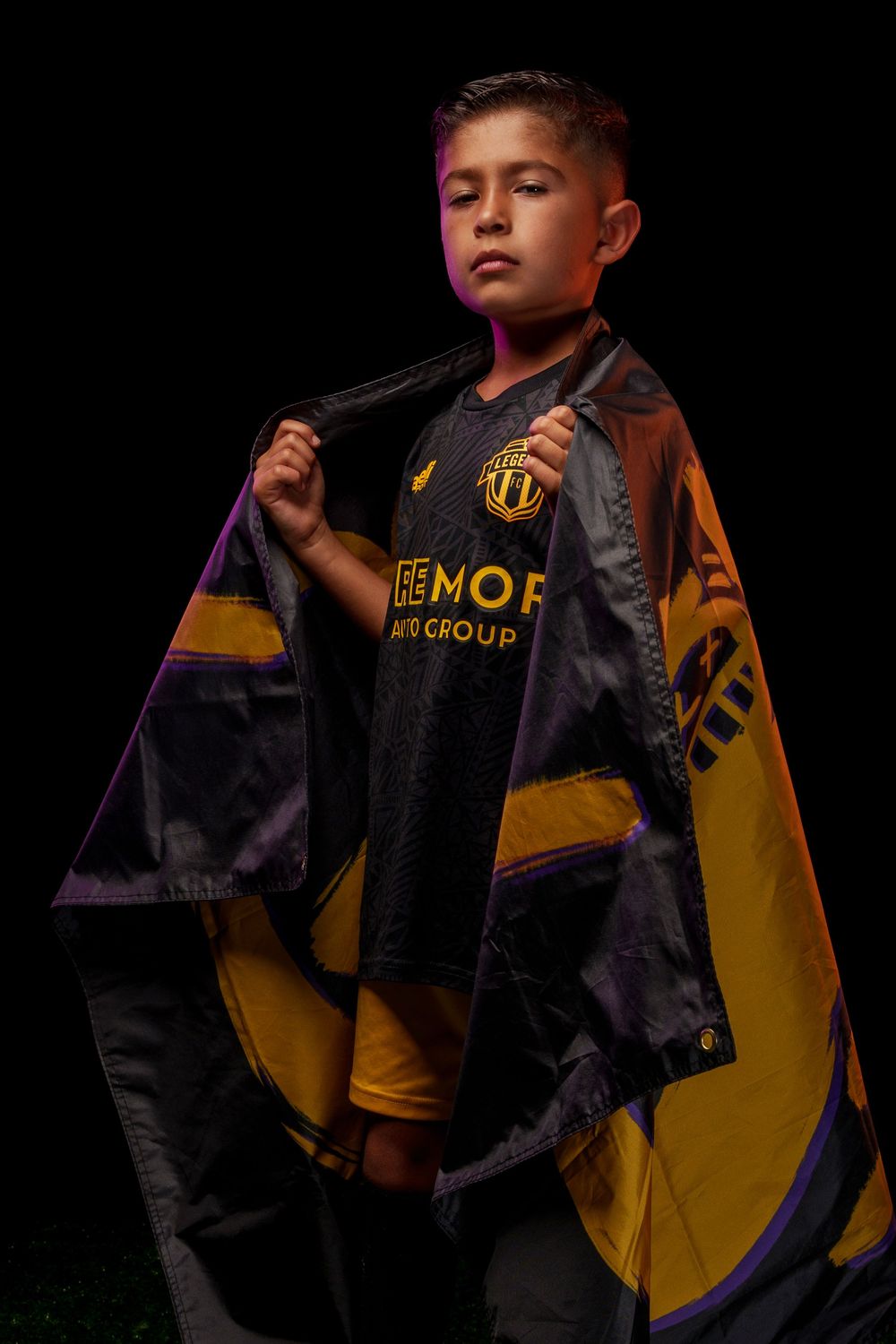 Young player in yellow and black uniform poses dramatically in dark studio setting.