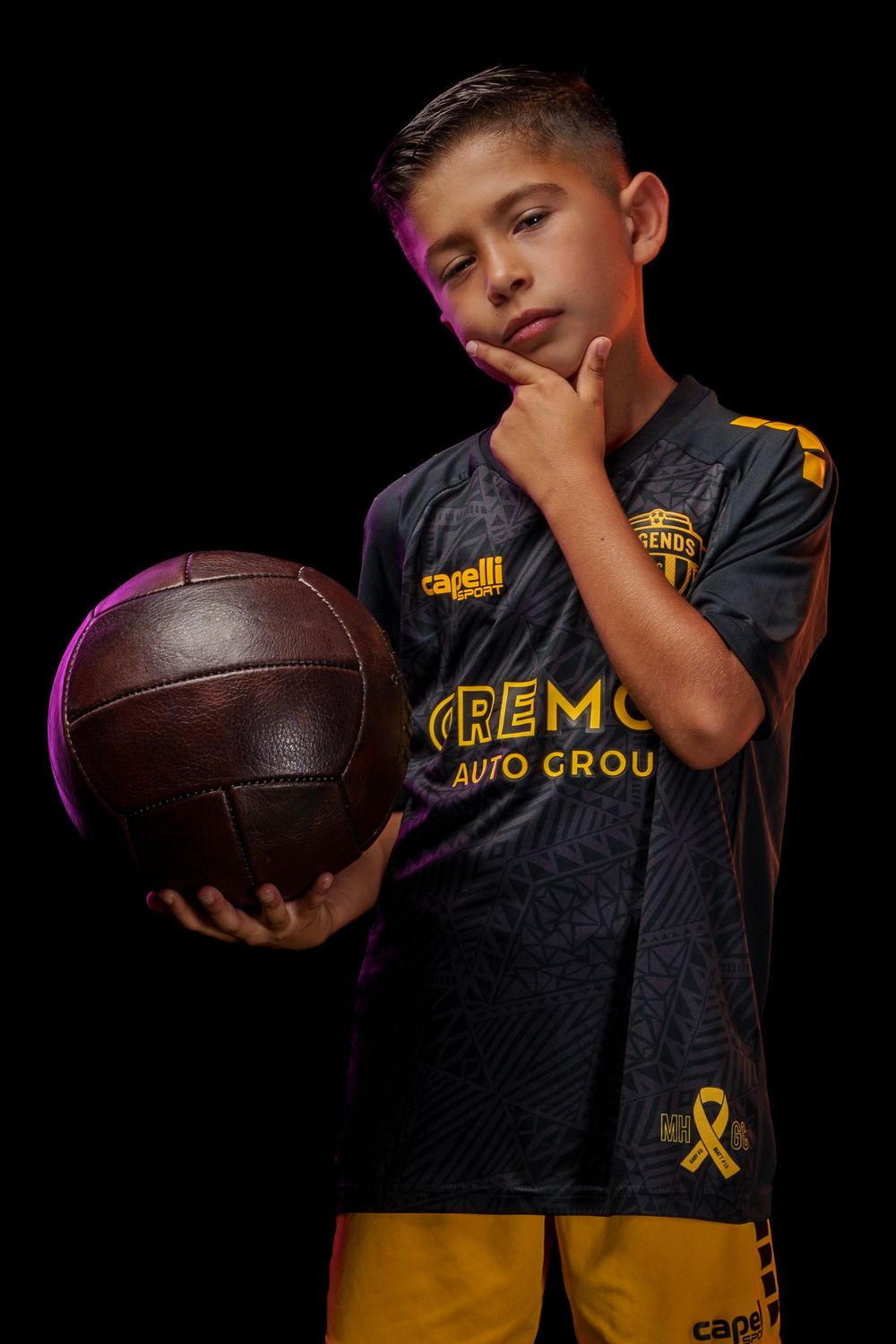 Soccer player poses with vintage-style football in dramatic studio lighting.