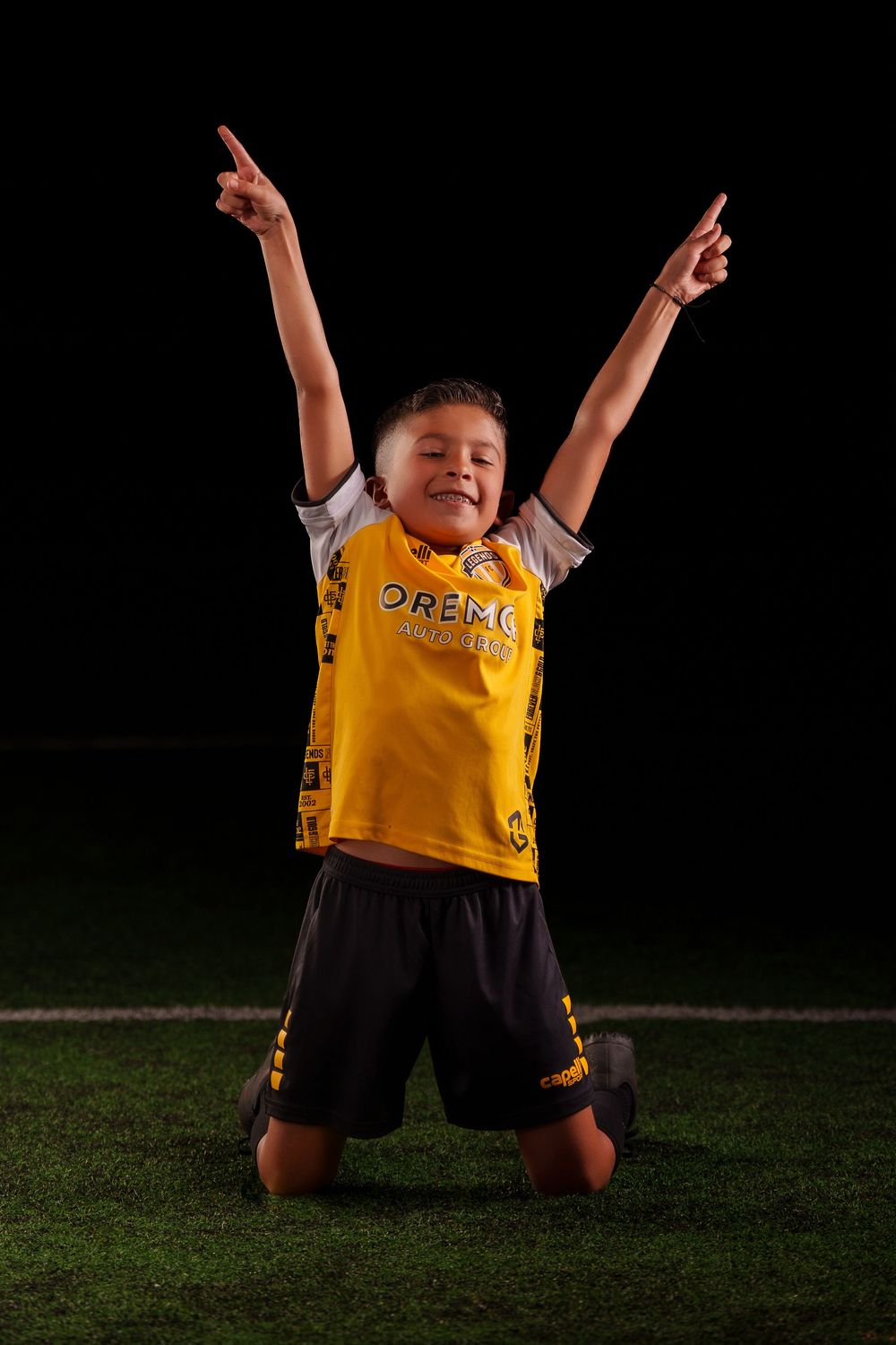 Soccer player celebrates with arms raised while wearing yellow jersey on dark field.