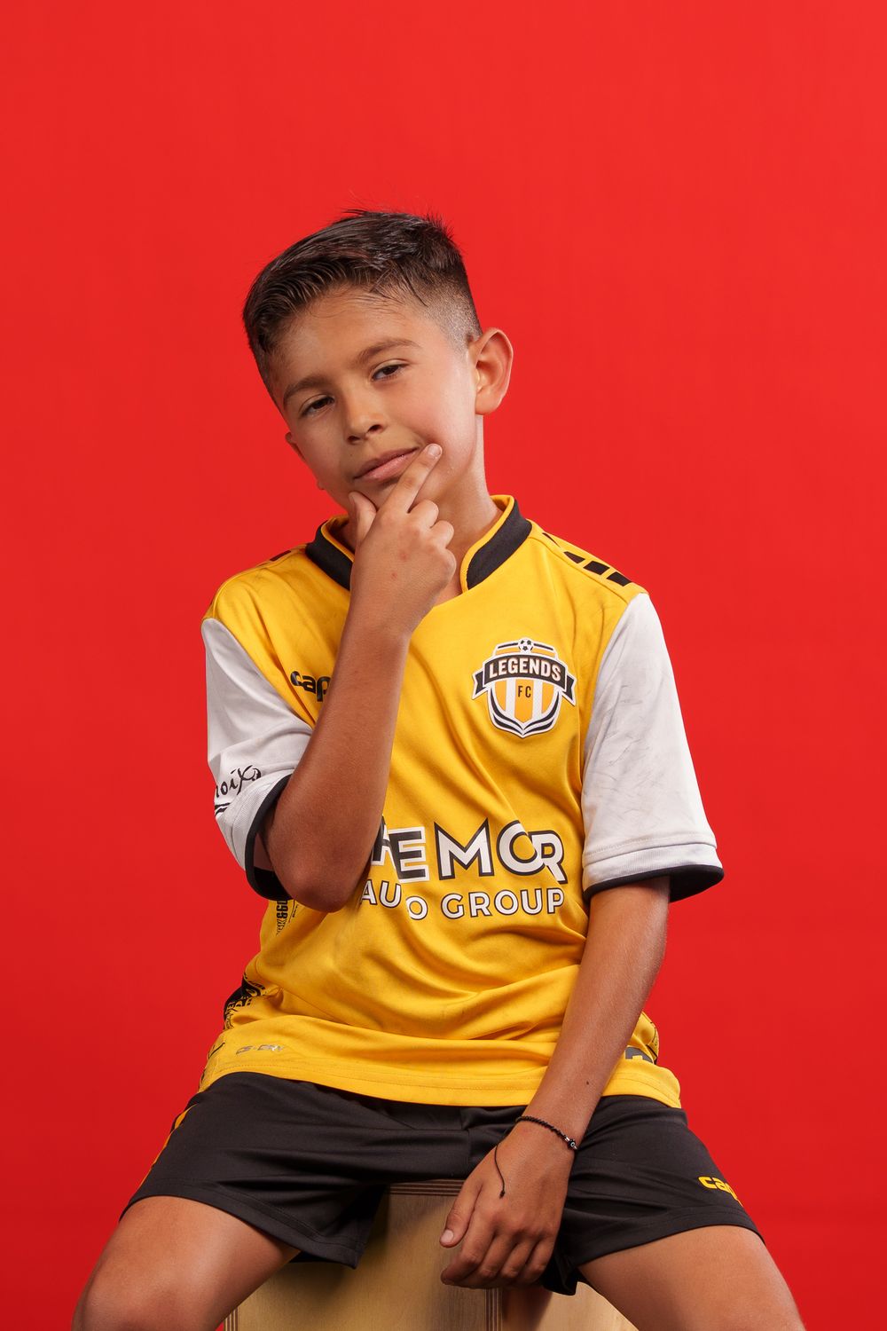 Young athlete sits wearing yellow Legends FC soccer uniform against vibrant red backdrop.
