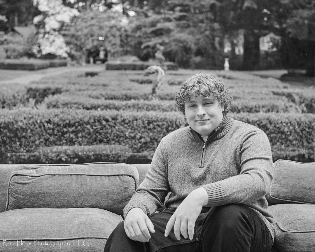 high school senior sitting on couch in mansion with garden behind him at Lakewold Gardens in Lakewold, WA