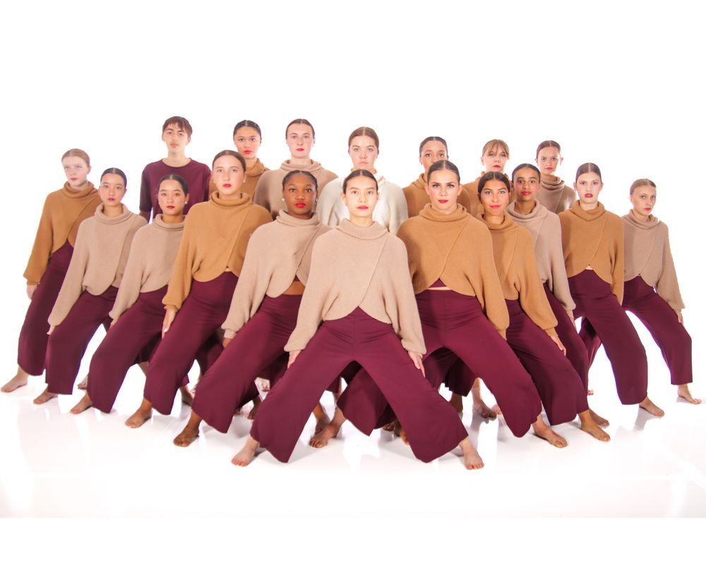 Dance company in burgundy costumes creates flowing horizontal line formation.