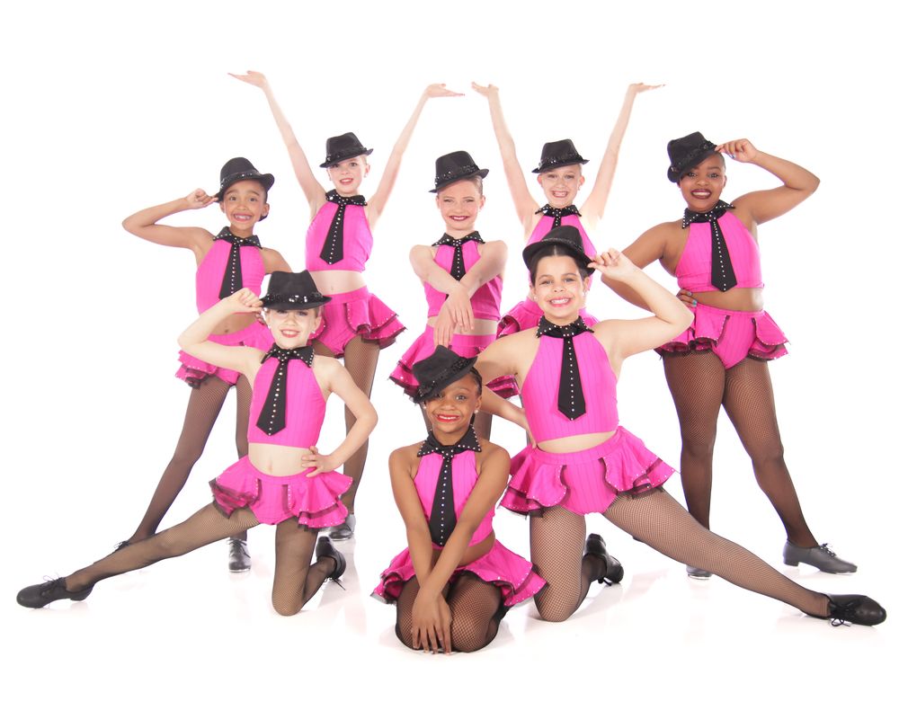 Dance performers in pink costumes and black bowler hats strike synchronized poses in a playful routine.