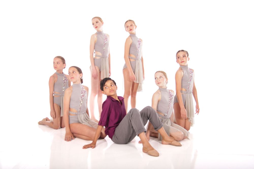 Dancers in gray leotards pose gracefully in a contemporary dance sequence against white background.