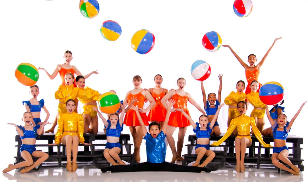 Group of performers with colorful beach balls create festive scene on stage.
