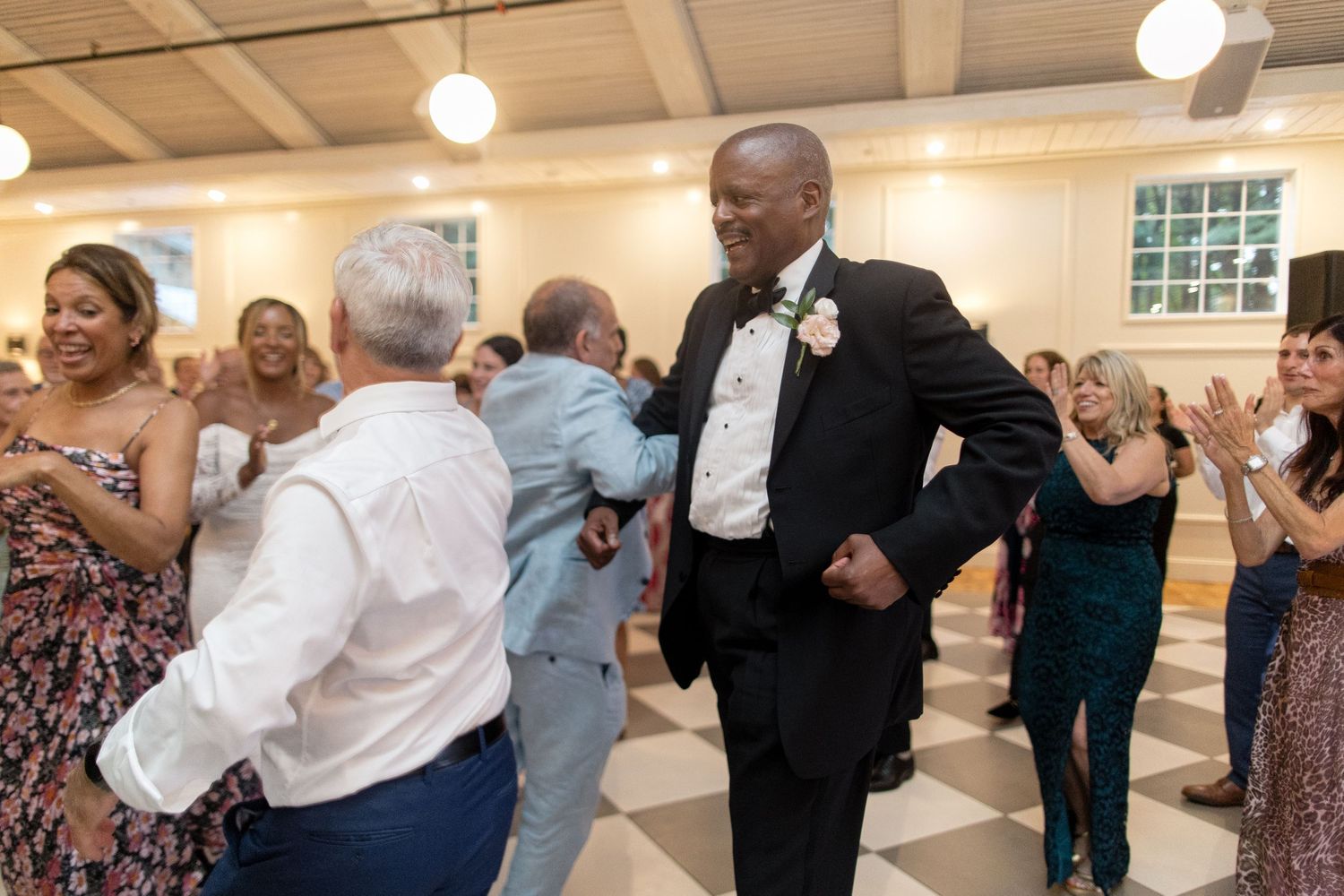 Wedding guests dance together and celebrate on a well-lit dance floor during an evening reception.