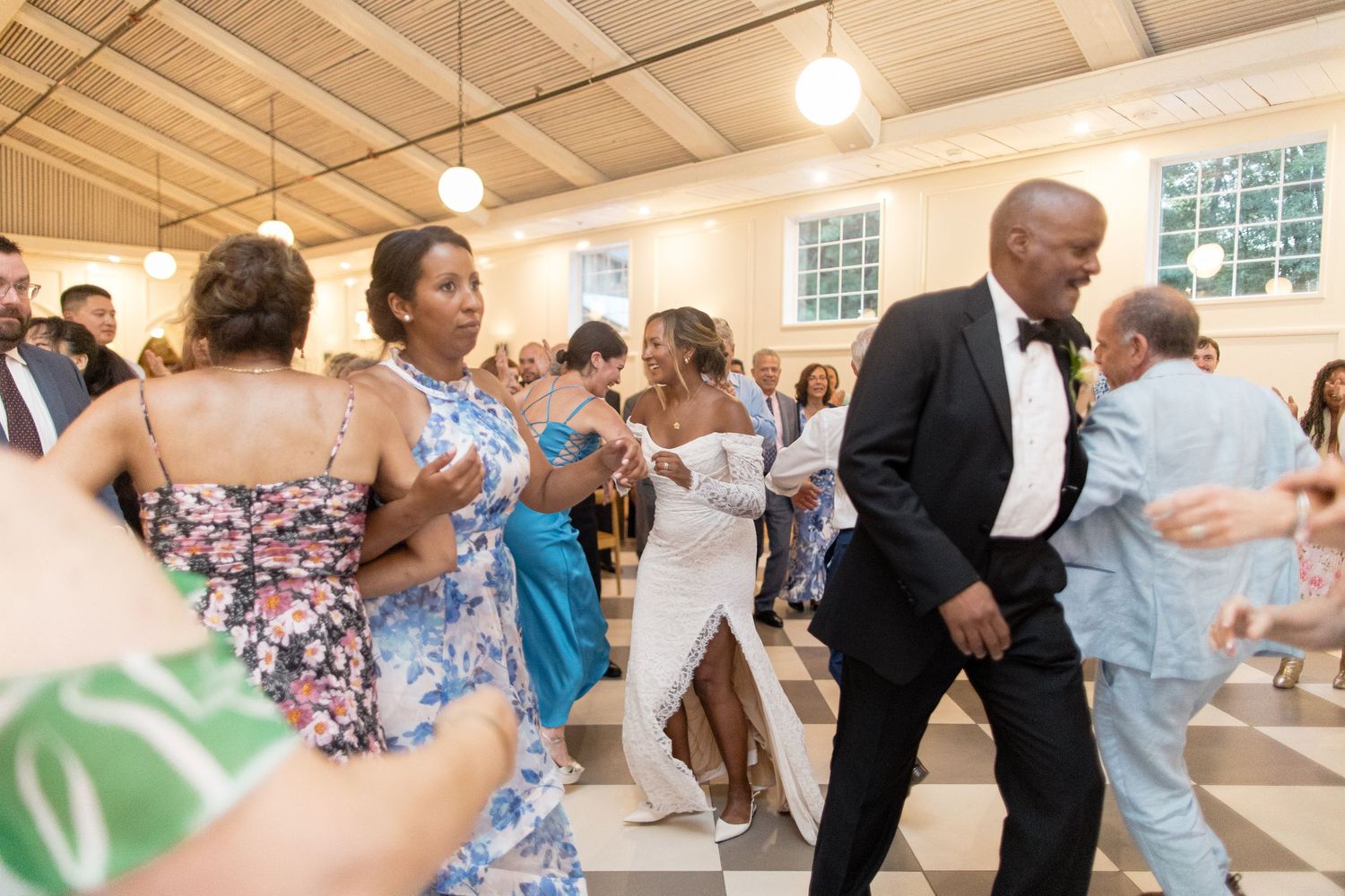 Wedding guests dancing and celebrating together in a bright reception hall space.