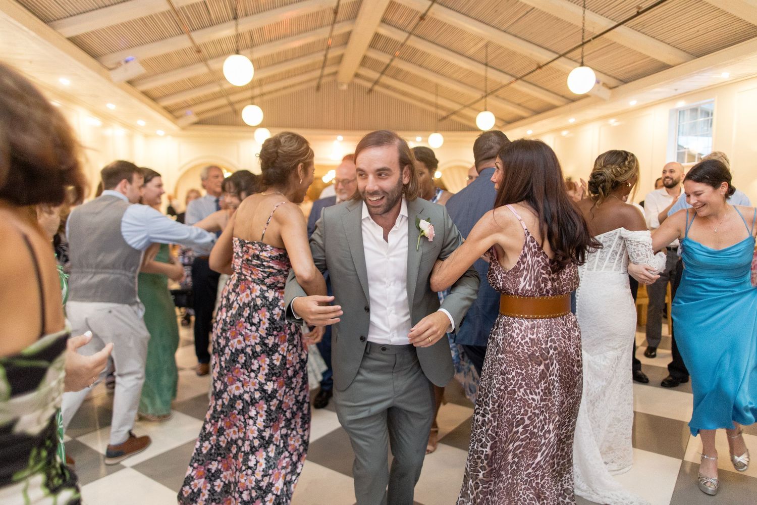 Guests enjoy dancing in a rustic reception hall with wooden beams and warm lighting for a wedding celebration.