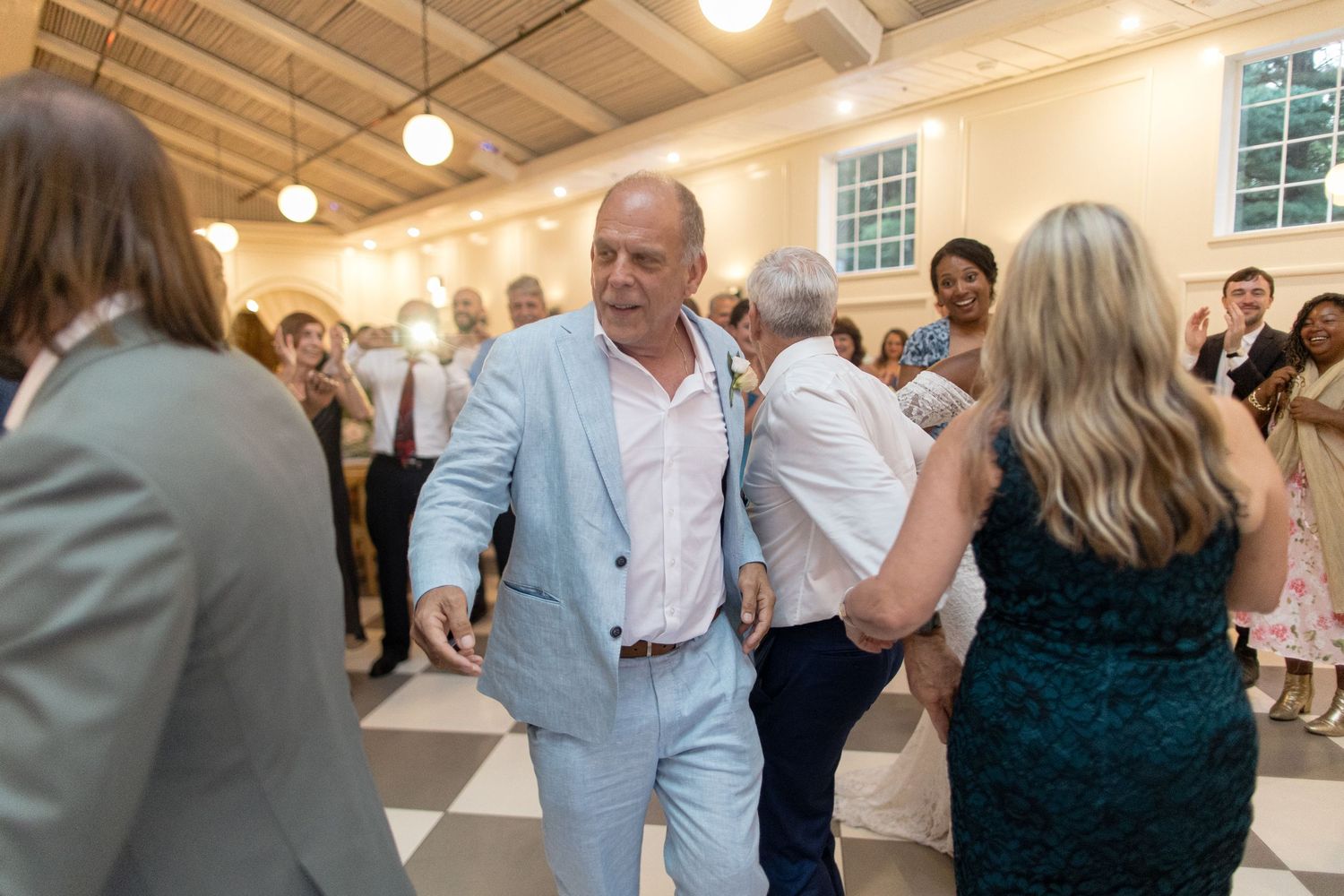 Wedding guests dancing and mingling in a bright indoor reception venue with pendant lights.