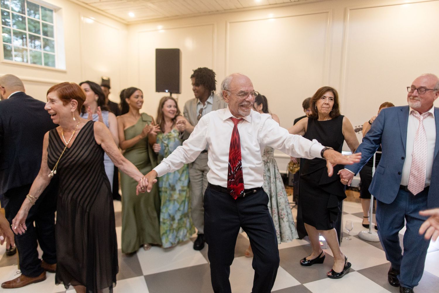 Wedding guests dancing and celebrating together in a bright indoor reception venue during a lively party.