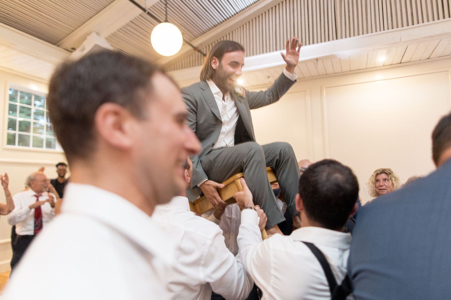 A group of jubilant business professionals celebrate with raised hands in an office meeting room.