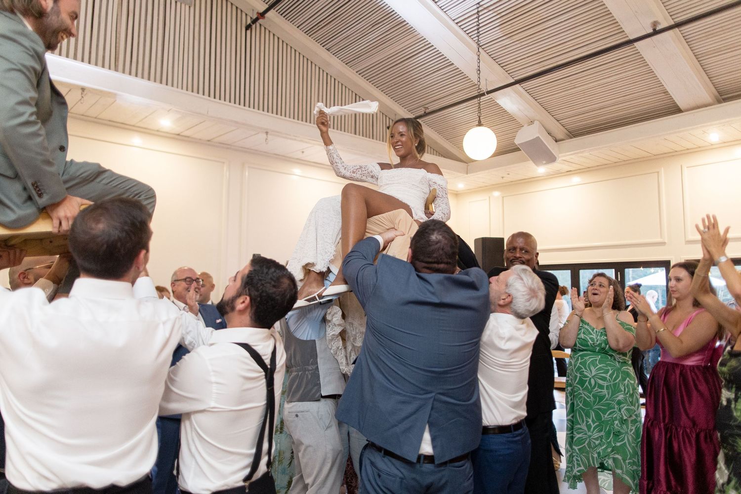 Wedding reception guests raise their hands in celebration while dancing together in a warmly lit venue.