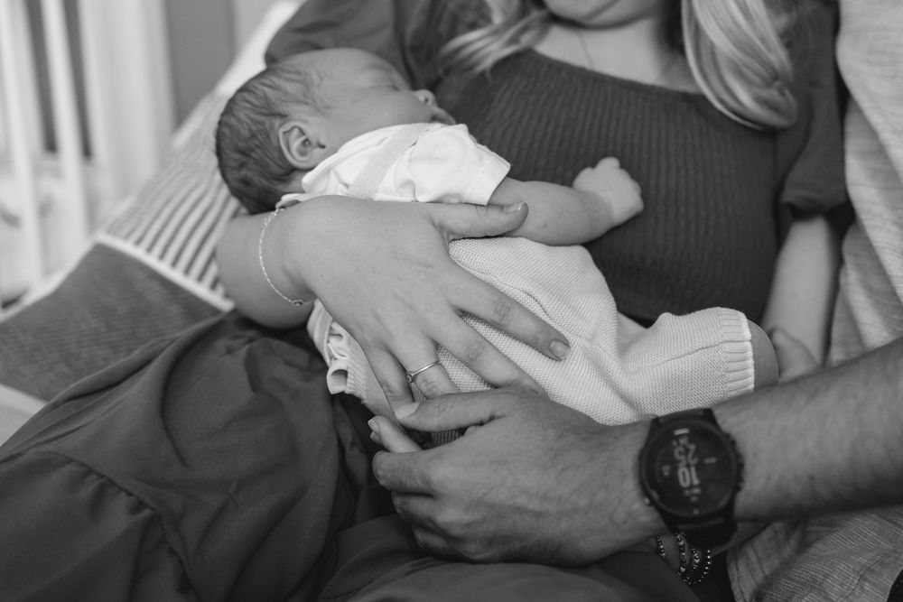Black and white photo showing baby lay in mothers arms, mother and father gently placed hands on baby
