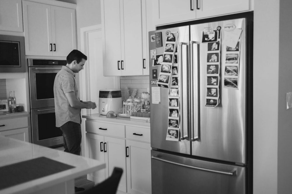 Black and white photo showing a man in a kitchen preparing baby bottle