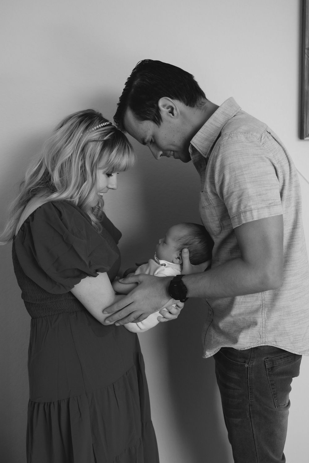 Black and white photo showing parents  touching foreheads and looking down at their newborn in tender moment of connection.